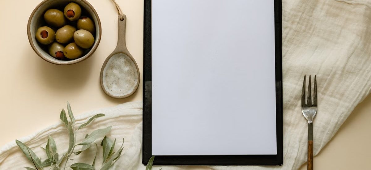 Flat lay of olives, a clipboard, and kitchen items creating a minimalist scene.