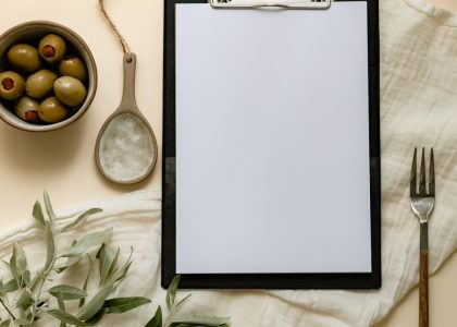 Flat lay of olives, a clipboard, and kitchen items creating a minimalist scene.